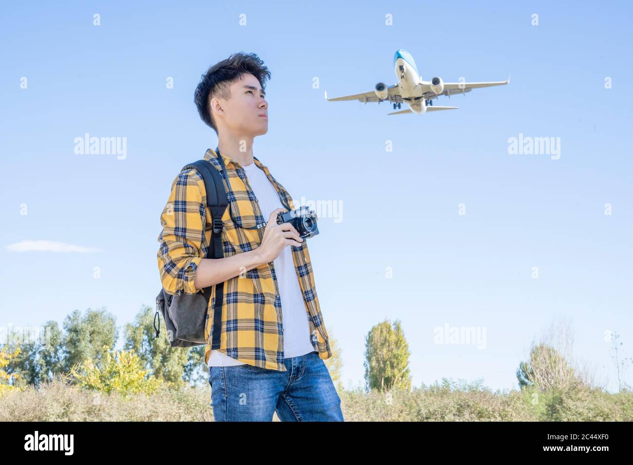 Giovane turista con macchina fotografica in natura con aereo sopra di lui Foto Stock