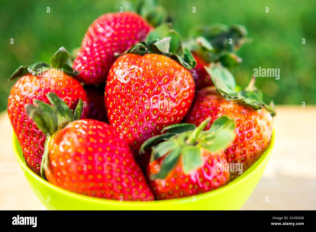 Fragole britanniche fresche in un recipiente su un asse di legno Foto Stock