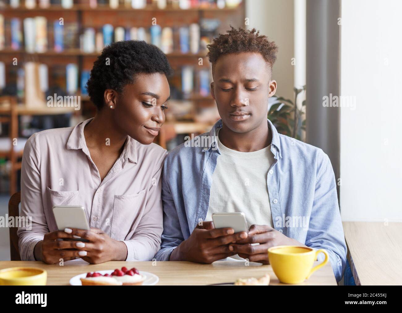 Dipendenza da Internet. Ragazzo nero millenario e ragazza che guarda i telefoni cellulari in data noiosa al bar Foto Stock