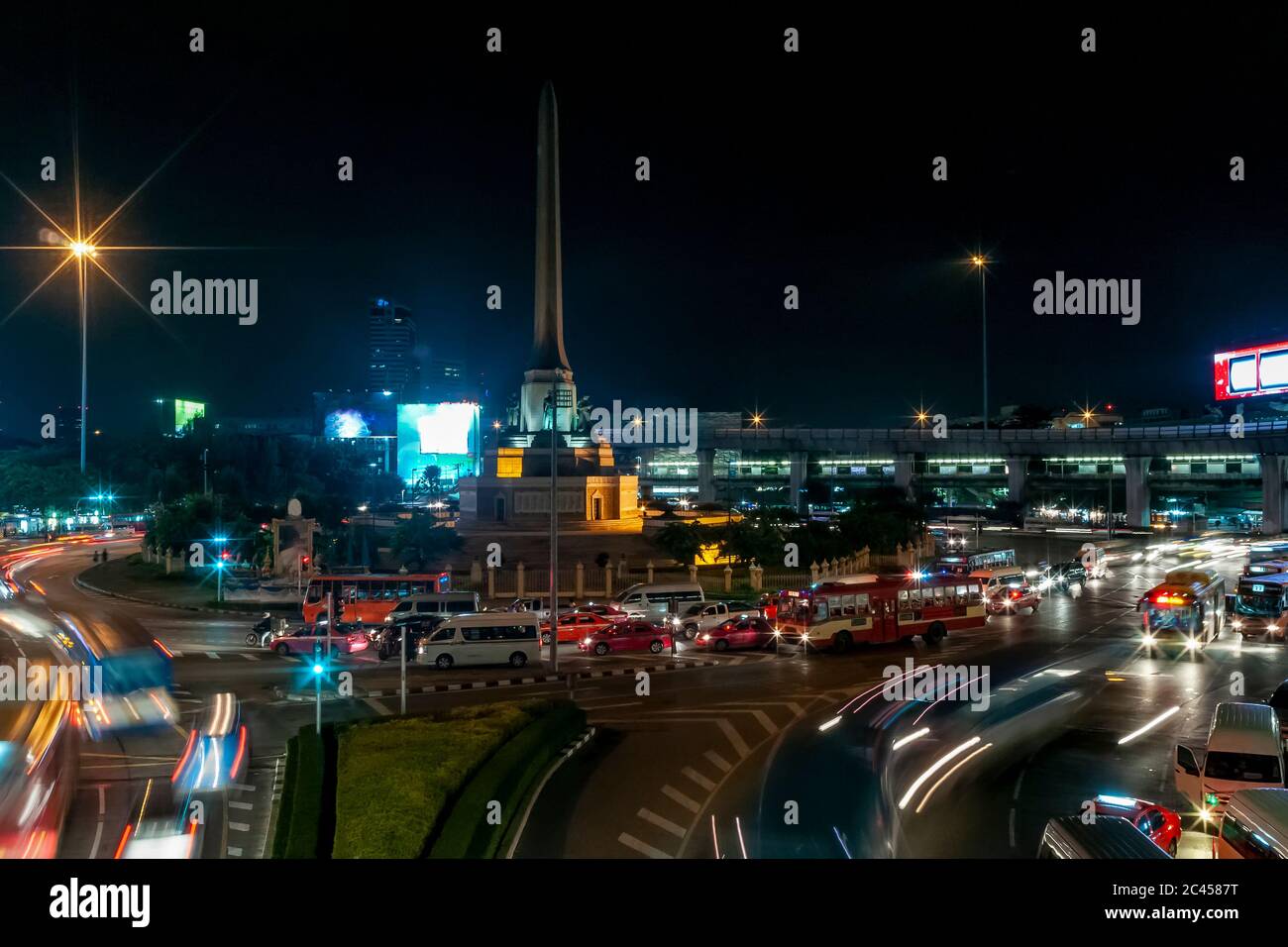 Vista notturna del monumento alla Vittoria nel quartiere Ratchathewi di Bangkok, Thailandia, con un sacco di traffico alla rotatoria Foto Stock