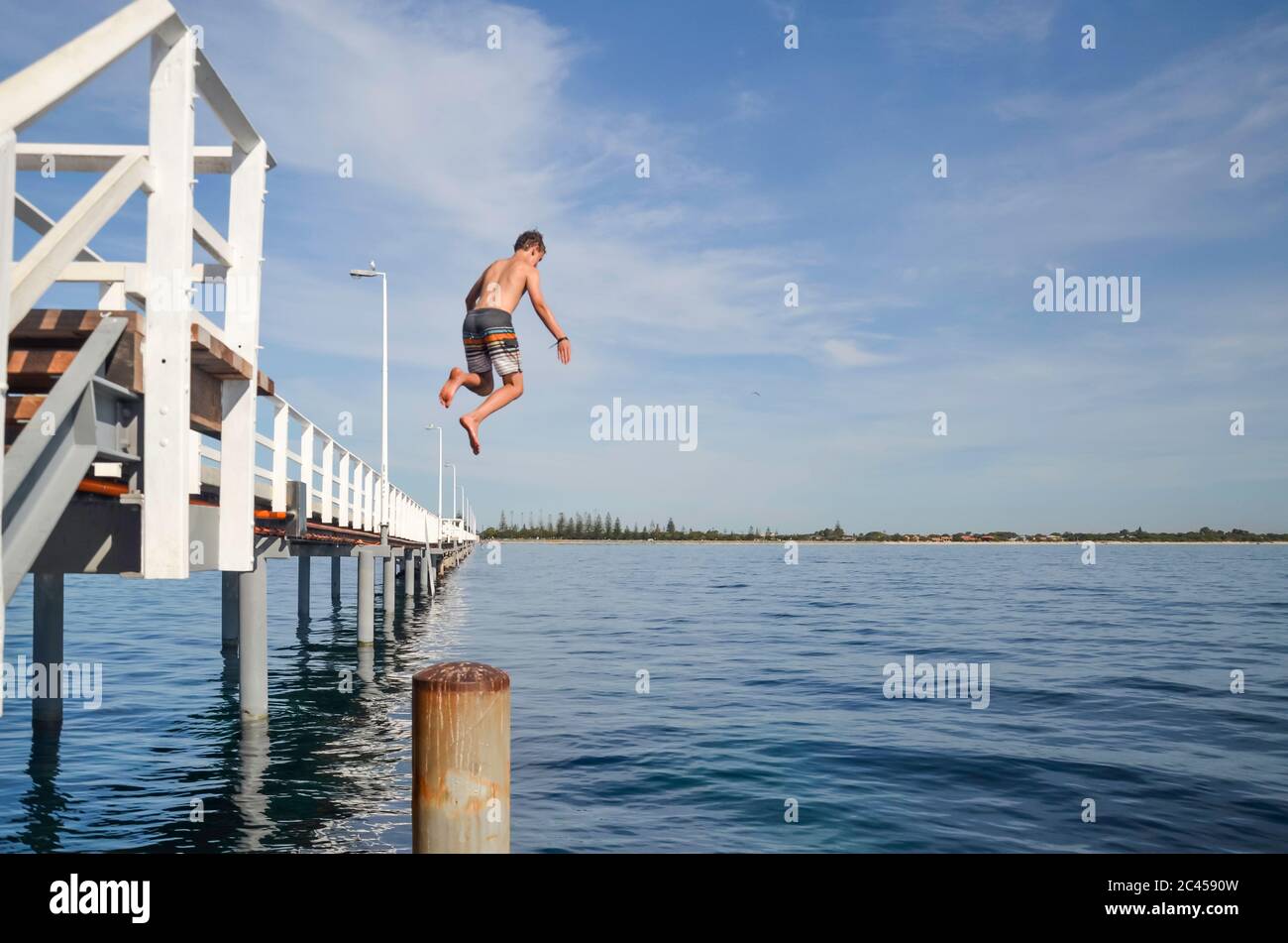 Un ragazzo salta dal molo Busselton lungo 1,8 km (il più lungo molo in legno in Australia) nella baia di Geographe nell'Australia occidentale Foto Stock