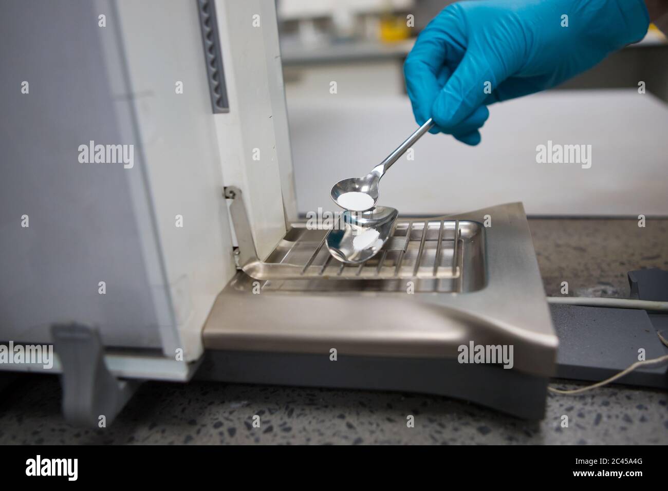 Chimico con mano a guanti che pesano un campione di polvere bianca su una bilancia analitica Foto Stock
