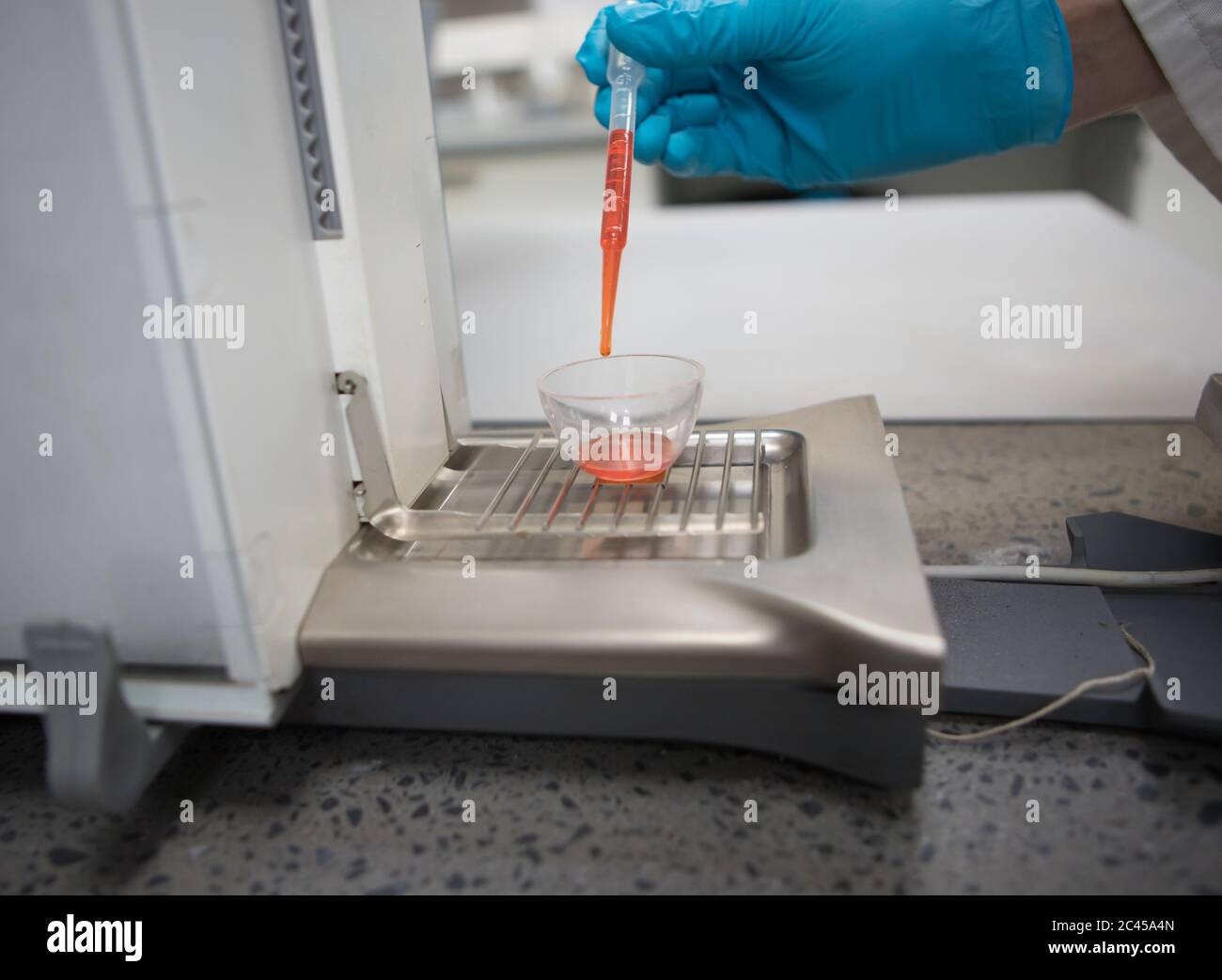 Chimico con mano a guanti che pesano una sostanza chimica arancione su una bilancia analitica Foto Stock