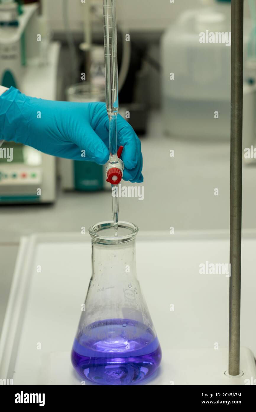 Scienziato in un laboratorio che esegue analisi chimiche mediante titolazione di soluzione blu. Mano con guanti Foto Stock