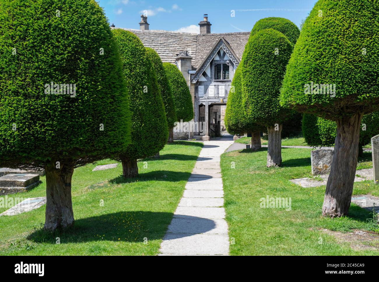 Chiesa di San Marys lychgate e tasso alberi alla luce del sole. Painswick, Cotswolds, Gloucestershire, Inghilterra Foto Stock