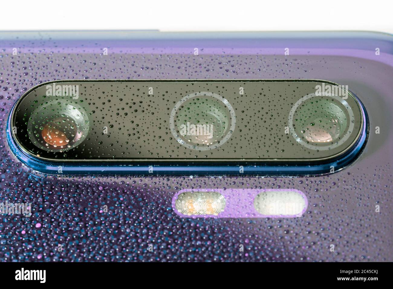 obiettivo viola della fotocamera del telefono coperto da piccole gocce d'acqua - primo piano con messa a fuoco e sfocatura selettive Foto Stock