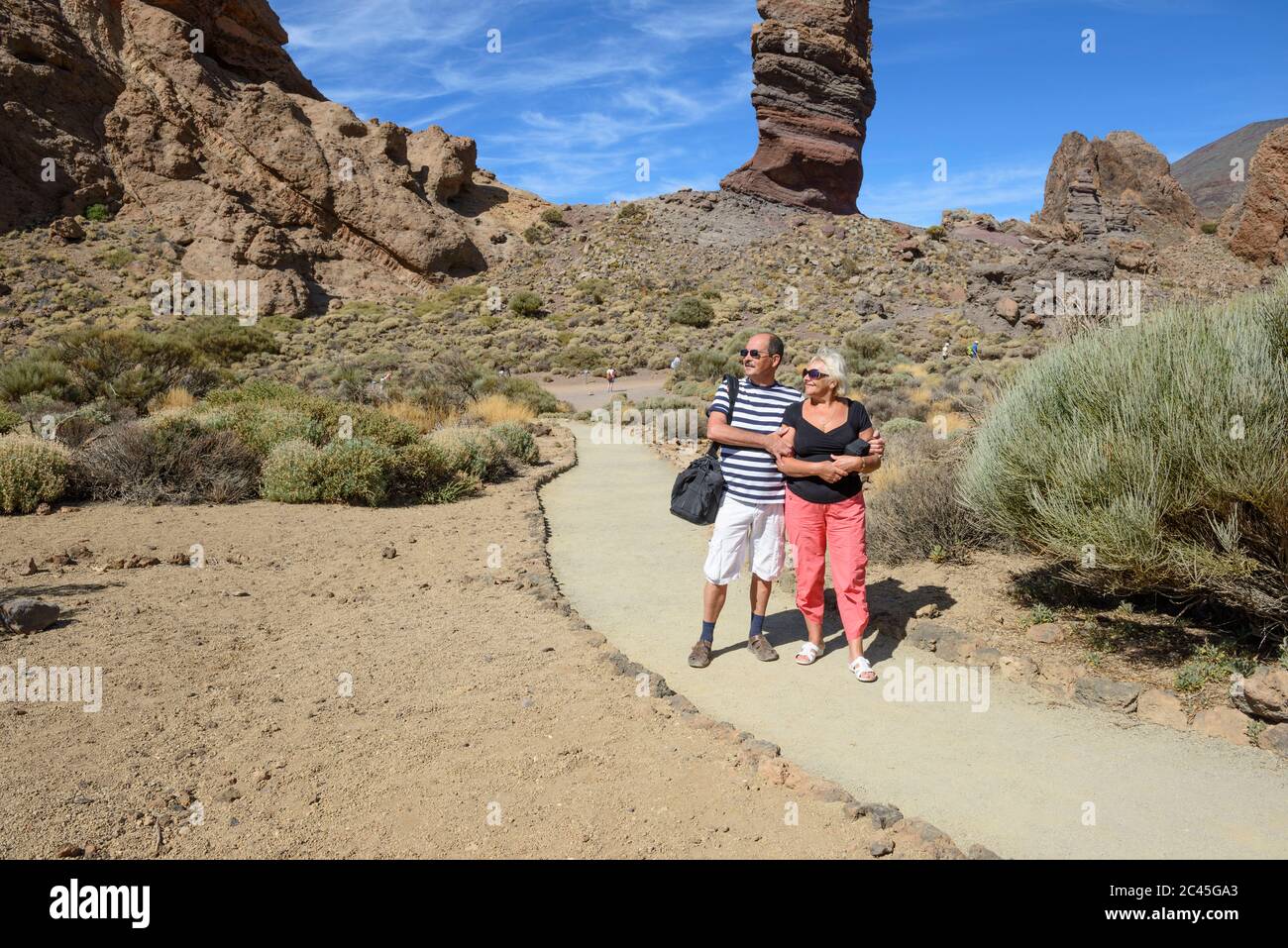 Coppie anziane si posano sul sentiero vicino Garcia Rocks con roccia di Cinchado sullo sfondo nel Parco Nazionale di Teide, Tenerife, Isole Canarie, Spagna. Foto Stock