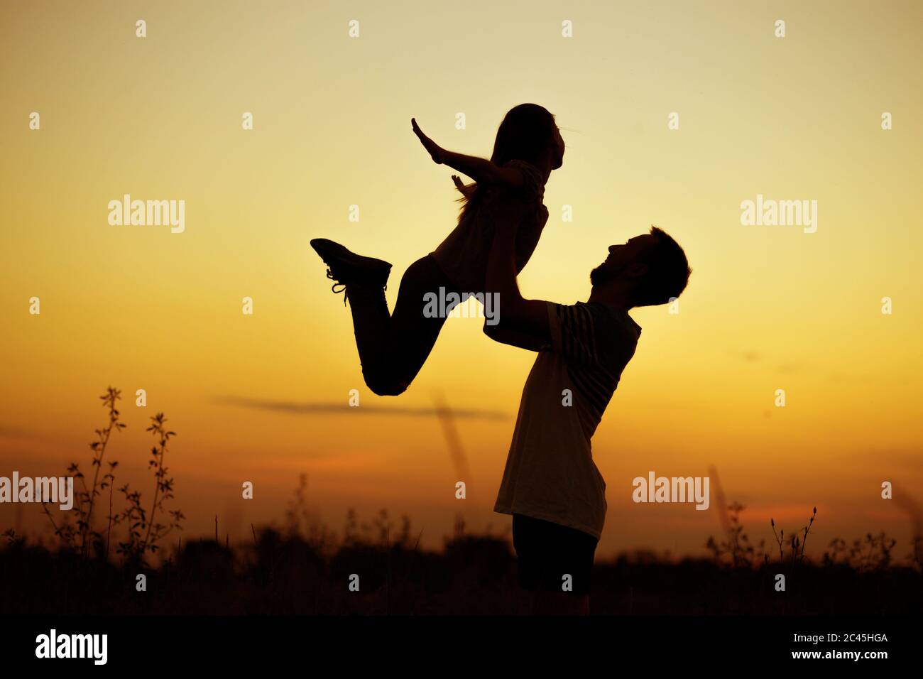 Silhouette di padre che getta la sua figlia felice nell'aria al tramonto. Famiglia togehter. Buon giorno del padre Foto Stock