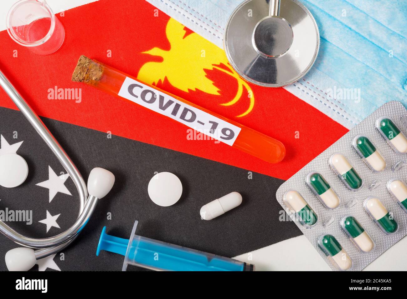Coronavirus, il concetto COVid-19. Vista dall'alto maschera respiratoria protettiva, stetoscopio, siringa, compresse sulla bandiera di Papua Nuova Guinea. Un nuovo focolaio o Foto Stock