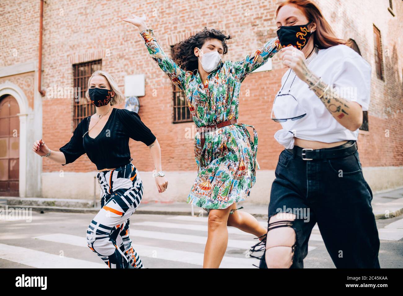 Tre giovani donne che indossano maschere di protezione durante il virus Corona, che attraversano una strada pedonale. Foto Stock