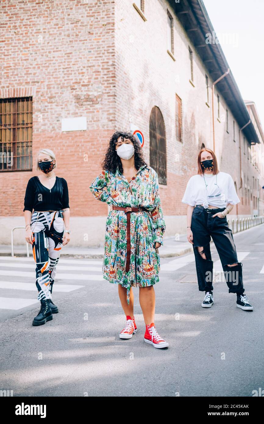 Tre giovani donne che indossano maschere di protezione durante il virus Corona, in piedi su un passaggio pedonale in una strada. Foto Stock