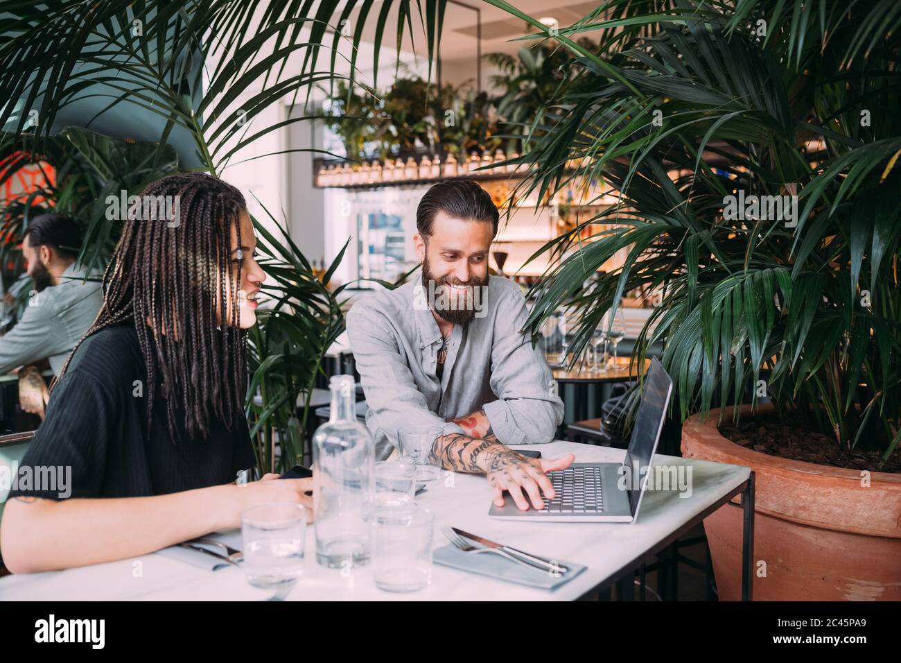 Giovane donna e uomo sopportato seduto ad un tavolo in un bar, guardando il laptop. Foto Stock