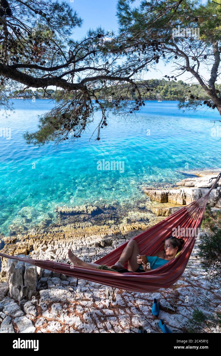 donna che invia sms con smartphone in amaca sull'isola di mljet, croazia Foto Stock