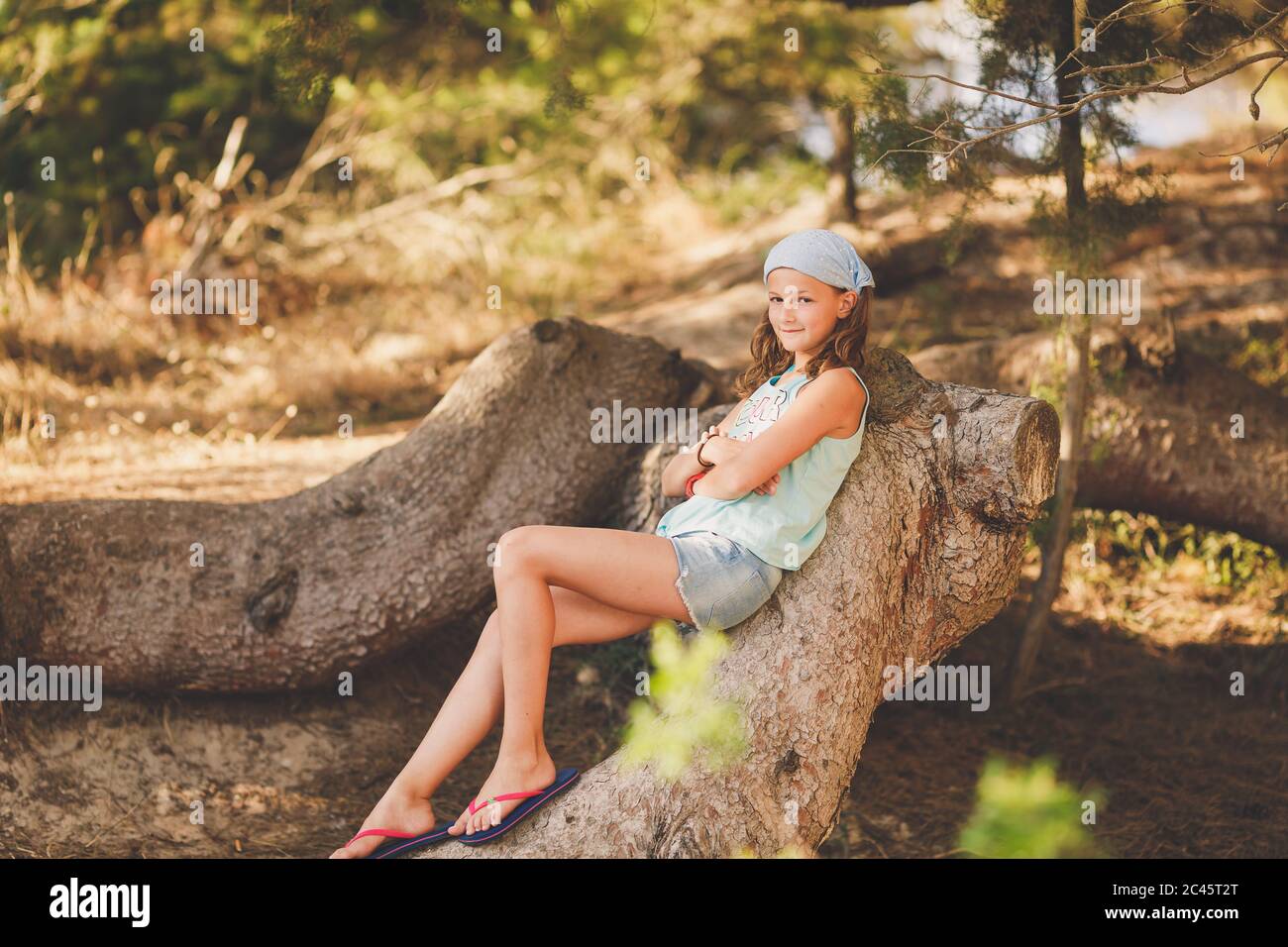 Una giovane ragazza seduta su un tronco d'albero in una serata soleggiata Foto Stock