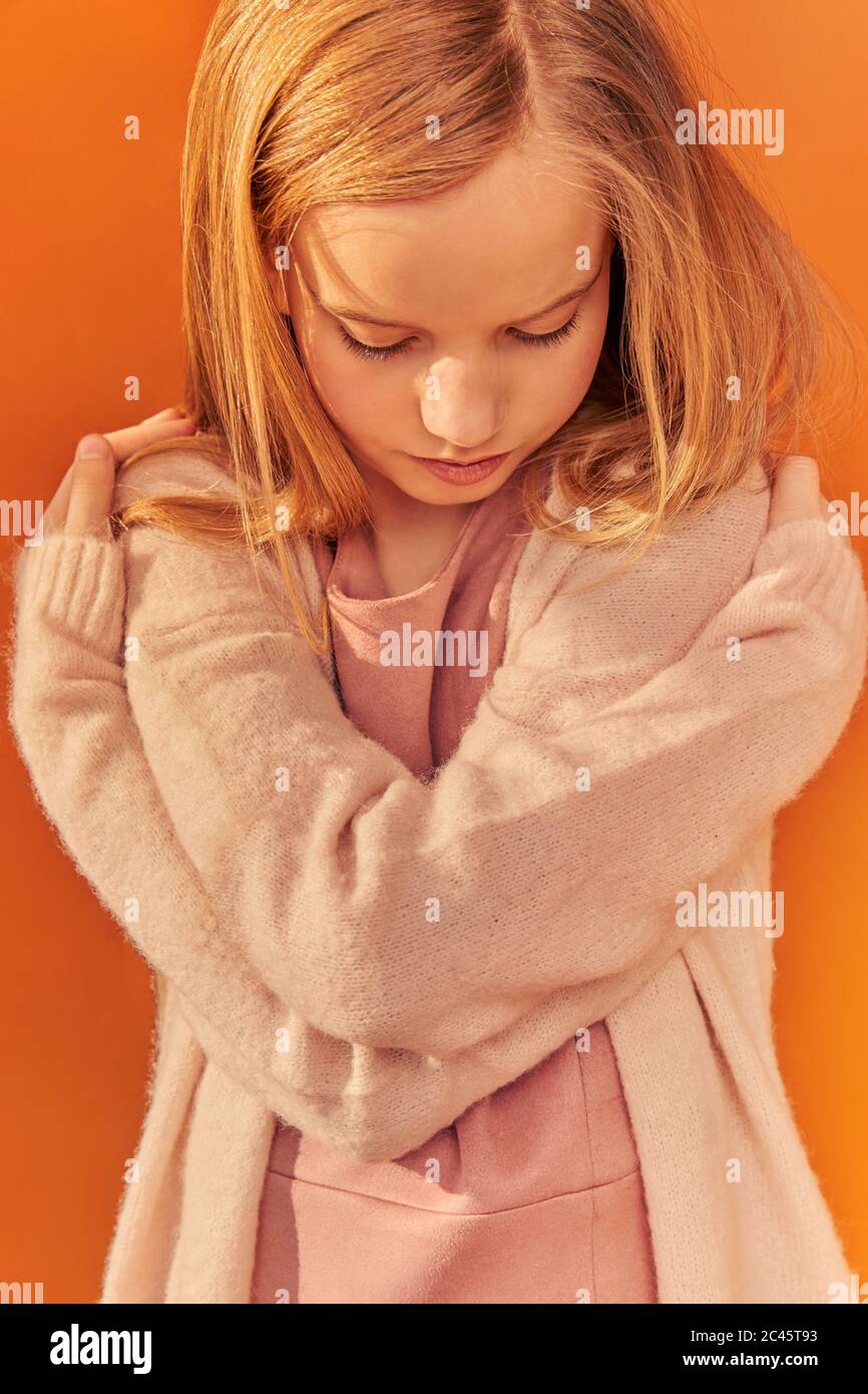 Ritratto di ragazza con lunghi capelli biondi che indossa cardigan color crema, su sfondo arancione. Foto Stock