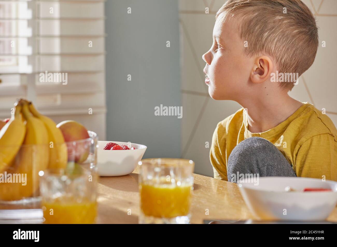 Ragazzo seduto al tavolo della colazione, guardando fuori dalla finestra. Foto Stock