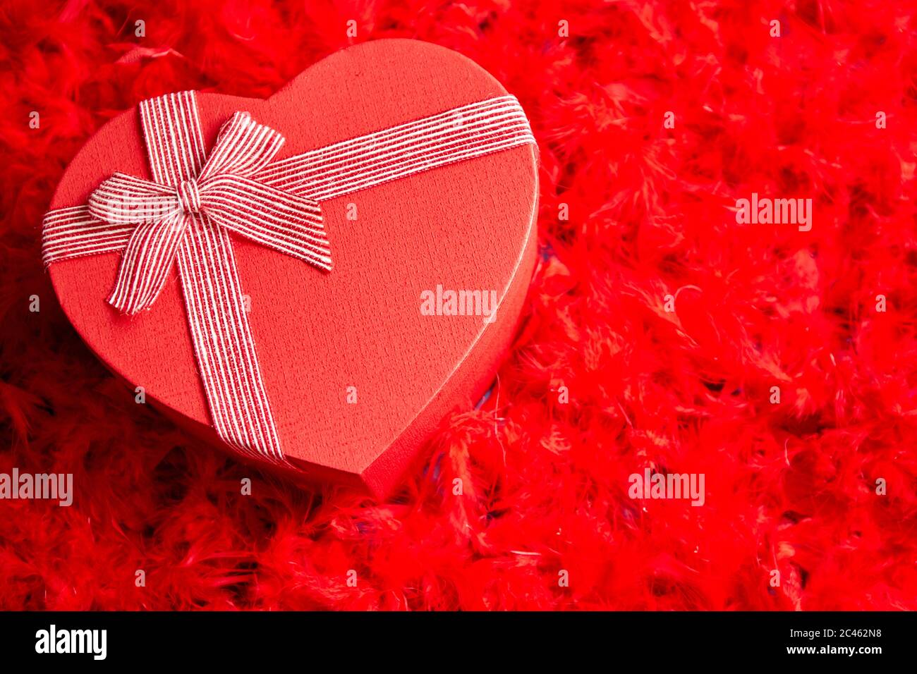 A forma di cuore regalo confezionato, posto sul rosso sfondo piume Foto Stock