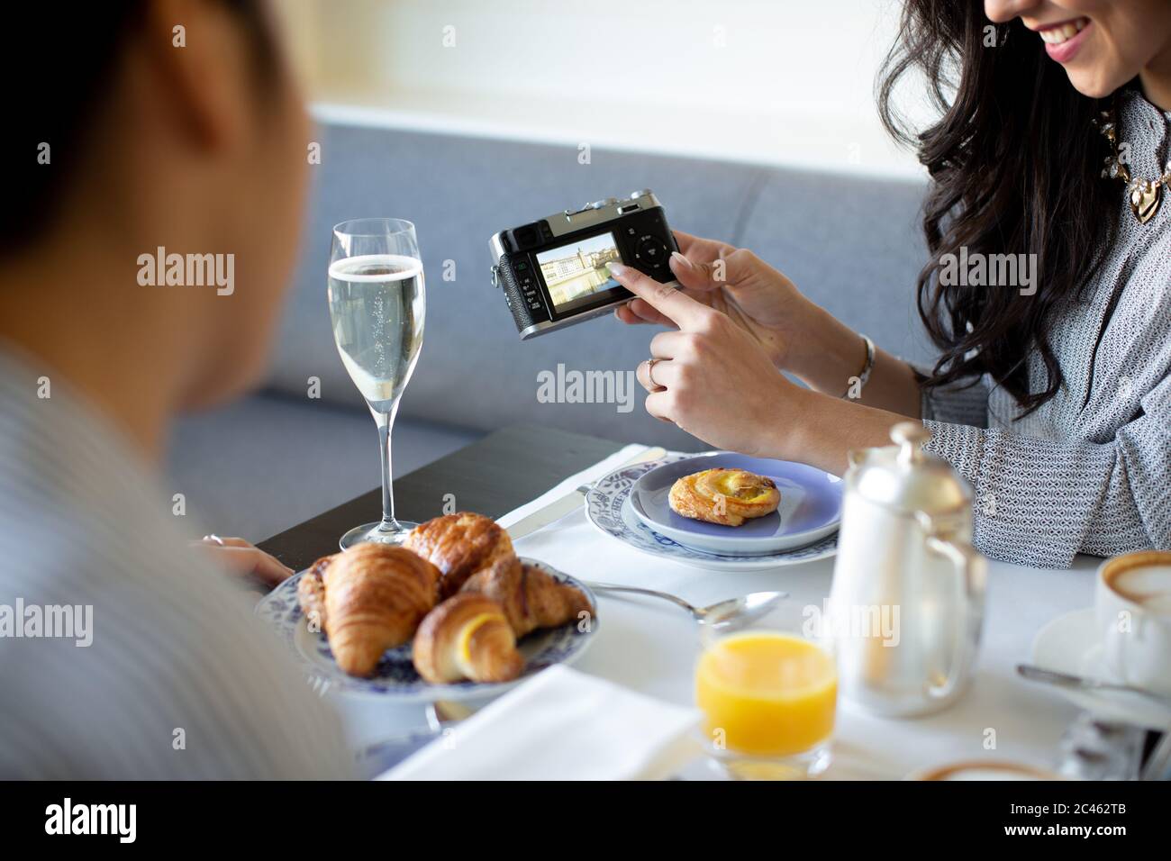Giovane donna puntando alla fotocamera digitale pur avendo prima colazione con champagne a boutique Hotel in Italia Foto Stock