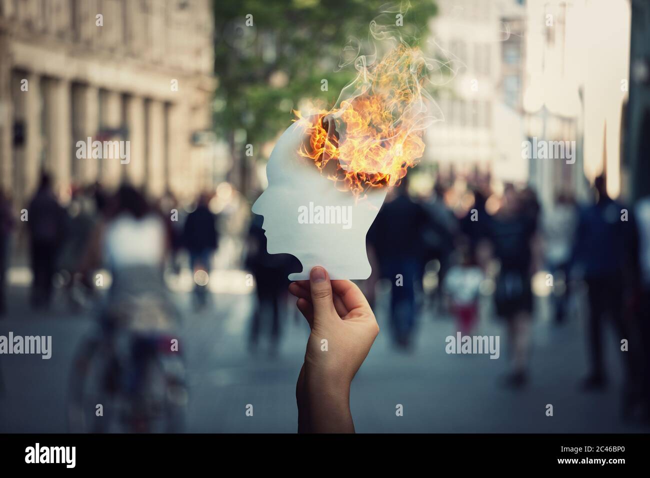 Burnout e concetto di stress come mano persona tiene un bruciante, testa umana a forma di foglio di carta su una strada affollata. Perdita di memoria e malattia di demenza. Alzhe Foto Stock