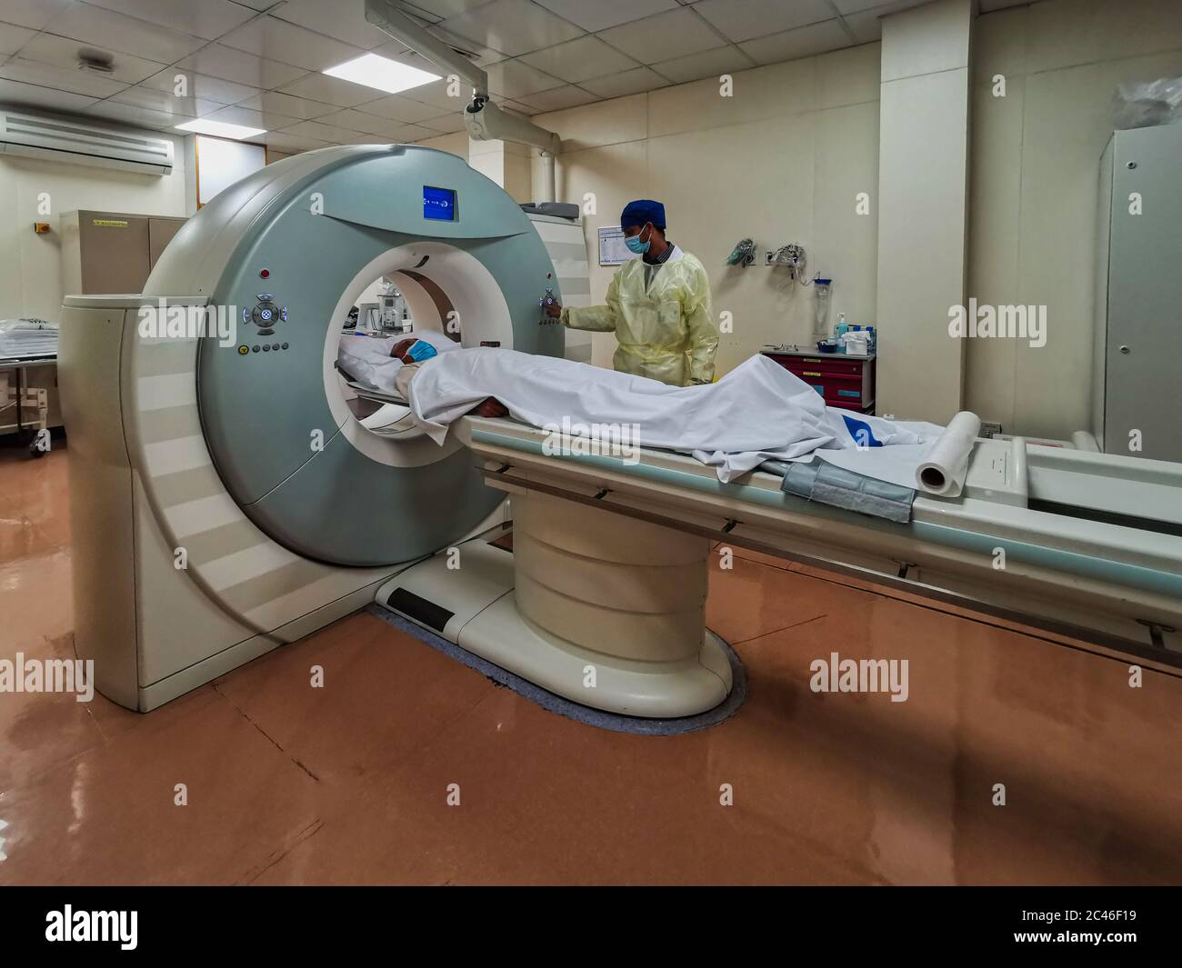 Macchina per tomografia computerizzata (CT) nel reparto di radiologia con tecnico di radiologia che indossa dispositivi di protezione individuale per la preparazione del paziente COVID-19 Foto Stock