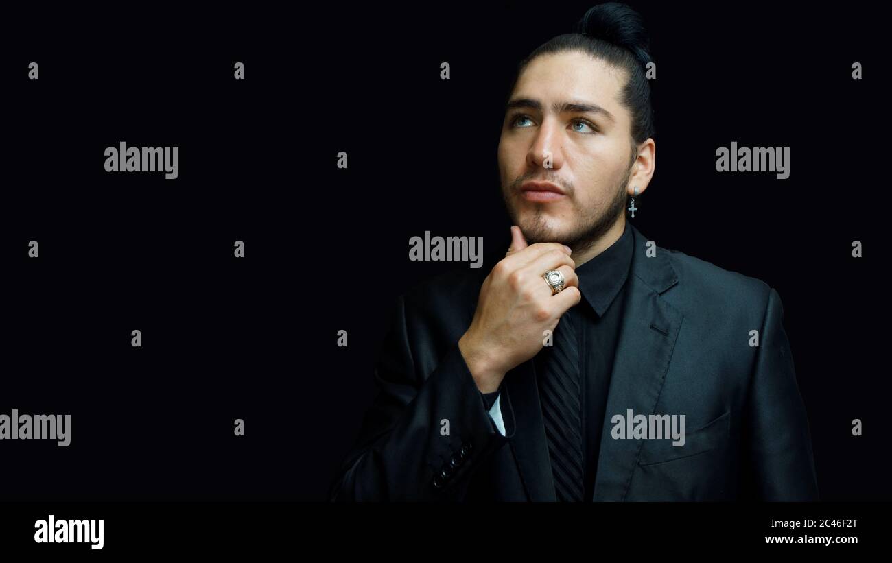 Giovane latino in abito nero, camicia nera, cravatta nera in posa premurosa  con la mano sulla mascella su sfondo nero Foto stock - Alamy