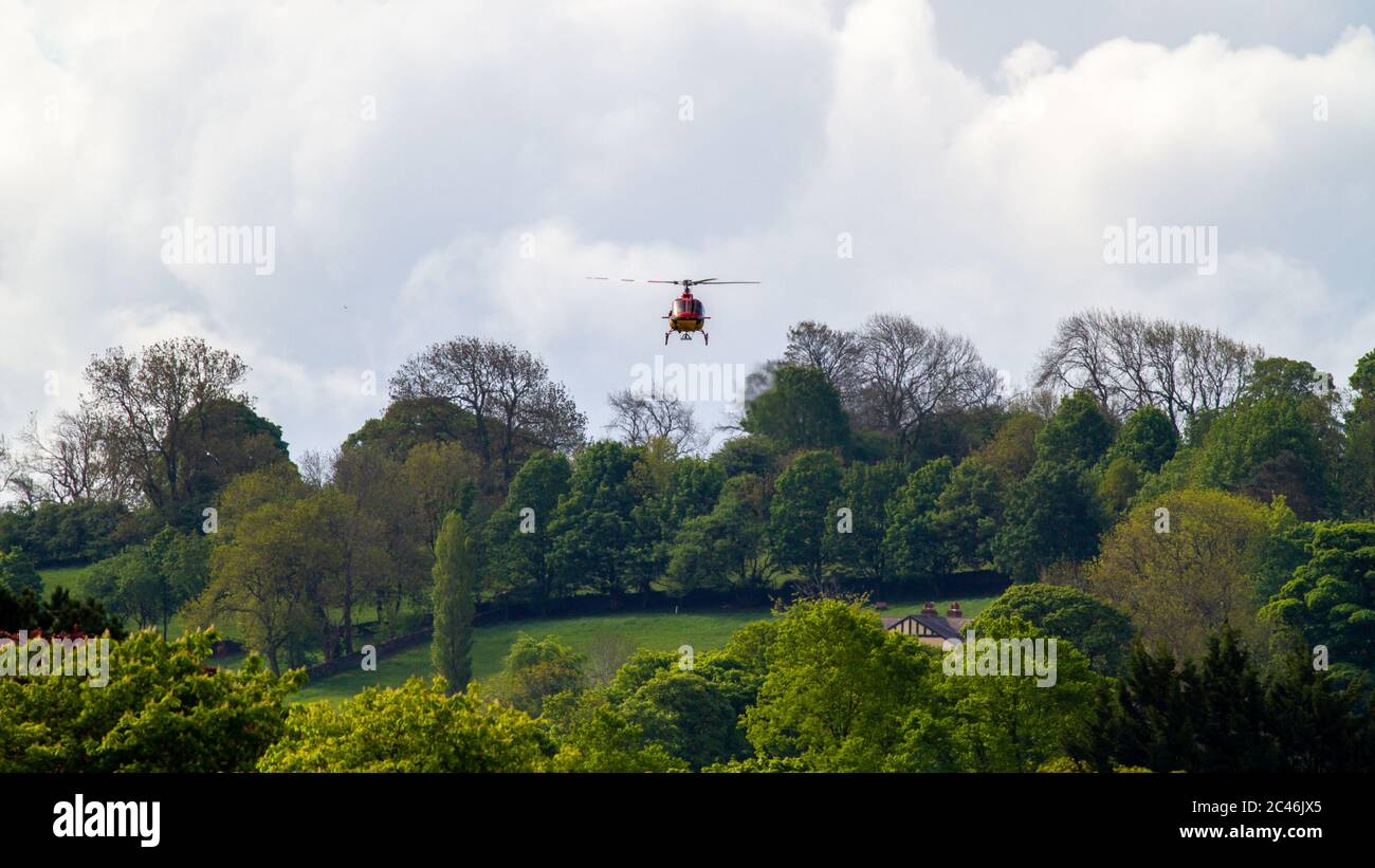 Elicottero rosso e giallo G ORKY che si aggirano verso le case vicine, Burley-in-Wharfedale, Regno Unito Foto Stock