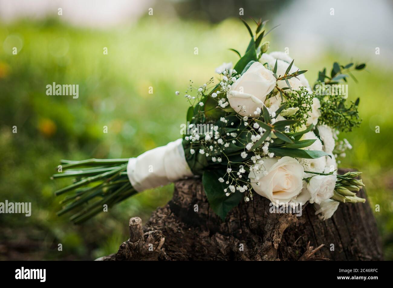Il bouquet di rose bianche e foglie verdi, splendidamente decorato con  nastro di raso bianco, giace sull'erba in una giornata estiva. Tema di  nozze Foto stock - Alamy