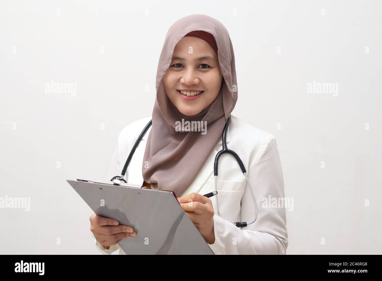 Asian musulmana femmina medico indossando hijab con stetoscopio in bianco cappotto tenendo appunti, pronto a servire il suo paziente medico, scrivere record medico di Foto Stock