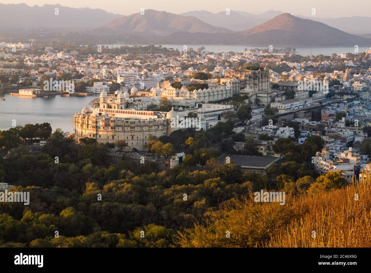 Vista aerea del Palazzo della Città e del Lago Pichola a Udaipur dal punto di osservazione di alta montagna al tramonto, con tonalità calde dell'ora d'oro. Rajasthan, India Foto Stock
