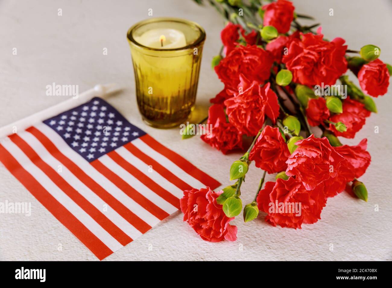 Bandiera americana e candela con fiori rossi garofano su superficie bianca. Veterans Day. Foto Stock