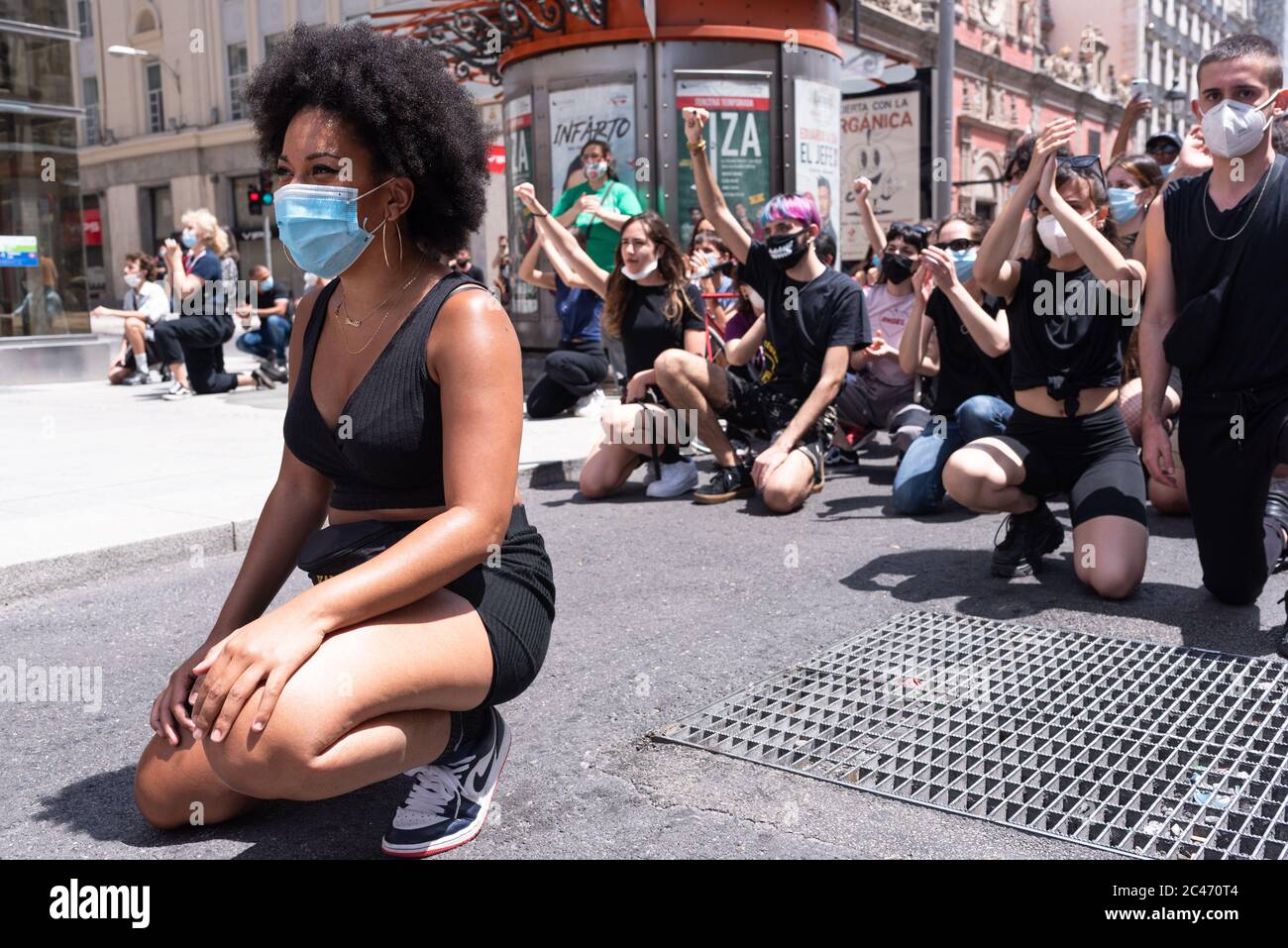 Ragazza nera con maschera inginocchiata in segno di protesta in Calle de Alcalá. Un gruppo di persone bianche la sostiene Foto Stock