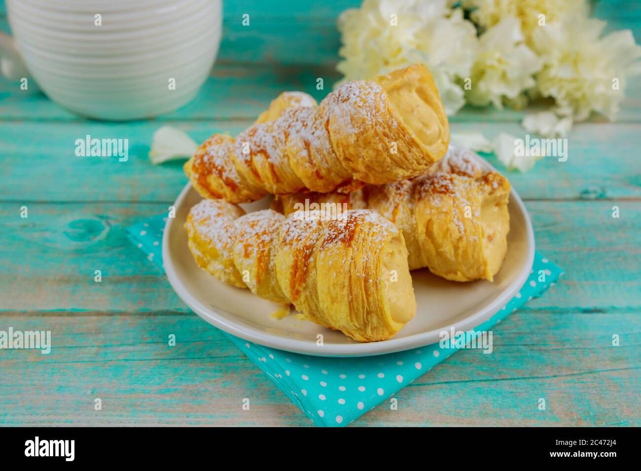 Tromba sfoglia con crema alla vaniglia e fiori su tavola di legno. Foto Stock
