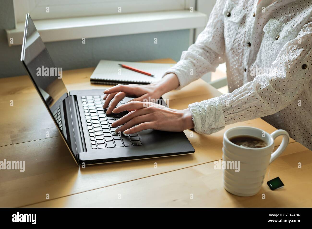 Le mani della donna che usano il computer portatile sulla scrivania all'interno della casa. Lavoro remoto. Freelance. Una tazza di tè, smartphone, notebook Foto Stock