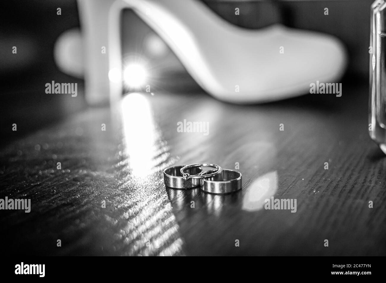 Tre anelli da sposa in oro e scarpe bianche con tacco alto sul tavolo Foto Stock