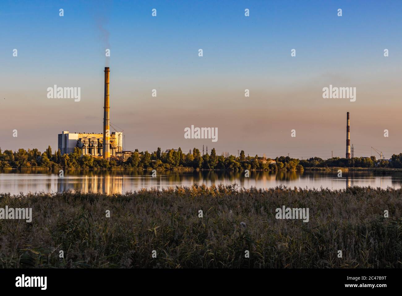 Vecchio impianto di incenerimento dei rifiuti con smokestack fumante sulla riva del lago. Il problema del trattamento dei rifiuti Foto Stock