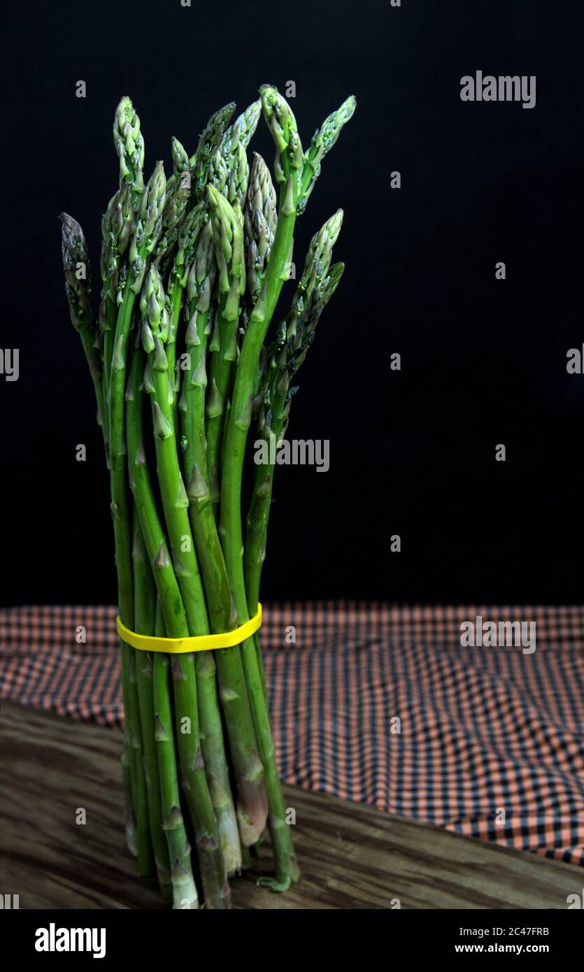 Primo piano di una manciata di asparagi selvatici su un tagliere di legno isolato su sfondo scuro Foto Stock