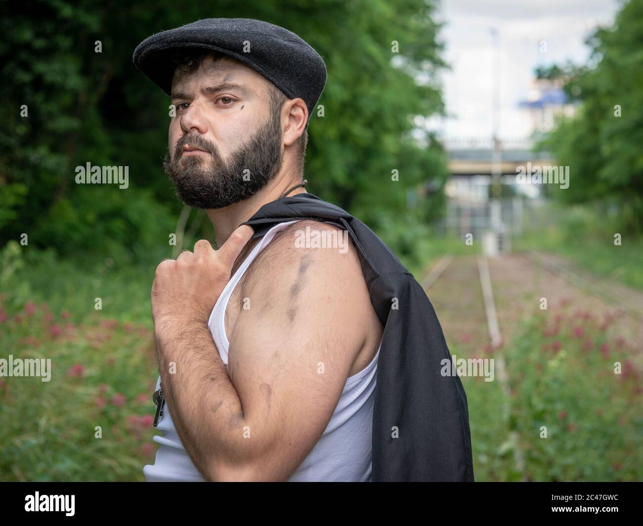 Giovane uomo francese bello bearded, con macchie di carbone sulla pelle, portato fuori su una pista ferroviaria disusata con fiori utilizzando la luce naturale in Par Foto Stock