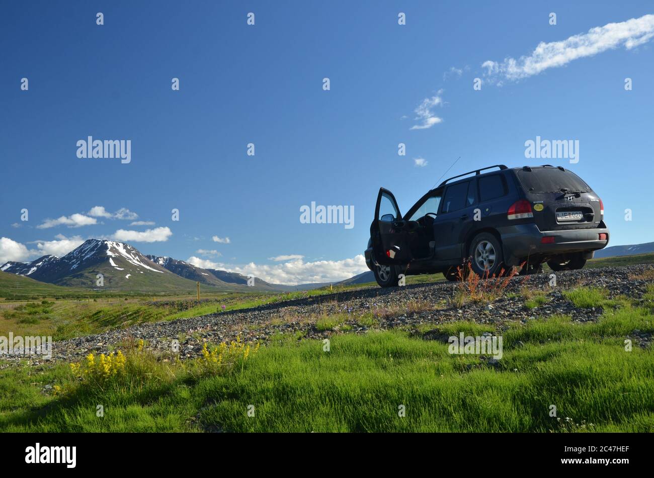 Auto sulla strada in cielo chiaro giorno in Islanda con le montagne sullo sfondo Foto Stock