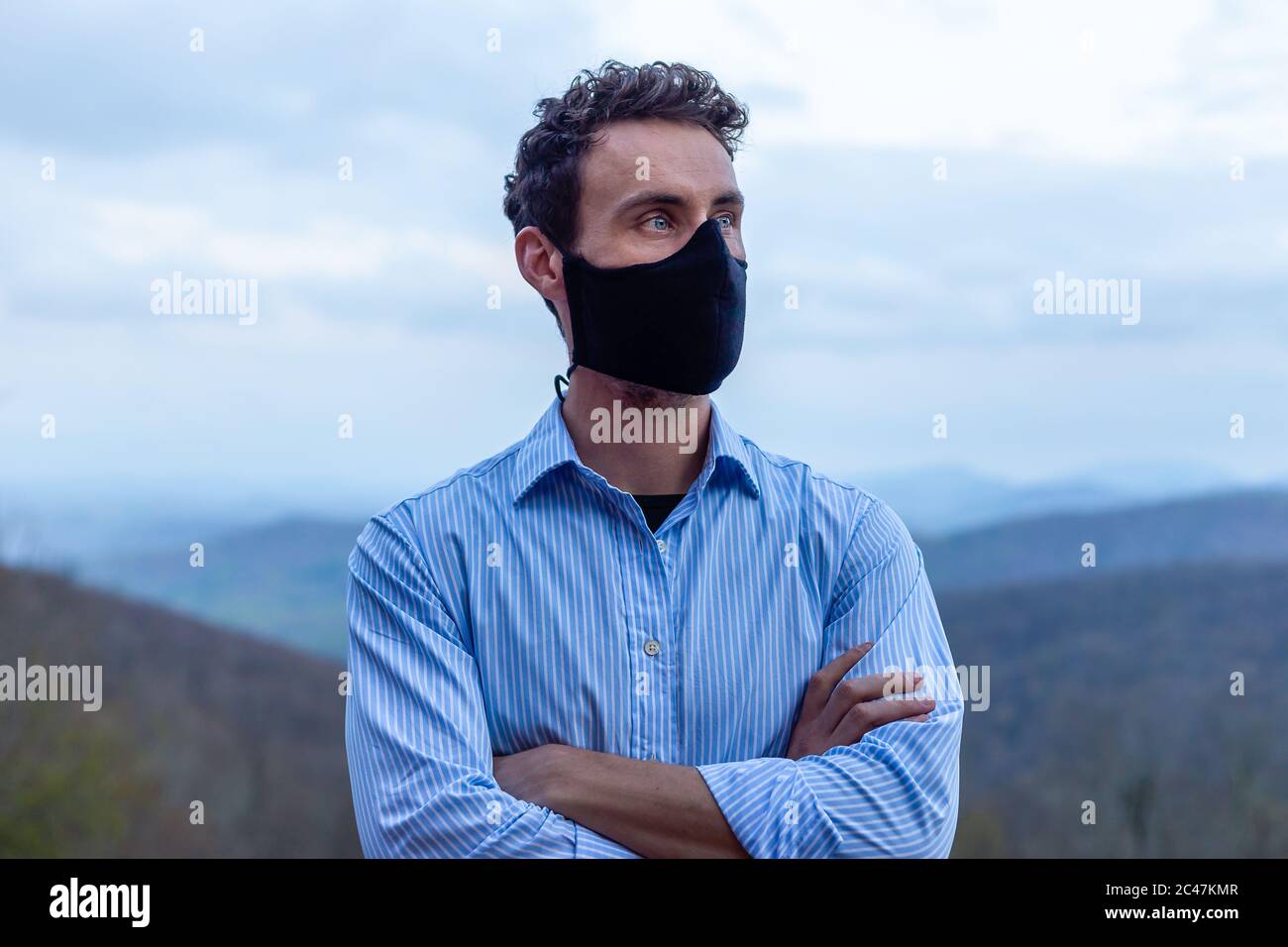 Giovane uomo che indossa maschera nera guardando con sicurezza nel futuro blu pulsante up camicia blu occhi marrone scuro capelli buona struttura ossea incrociati braccia ricche Foto Stock