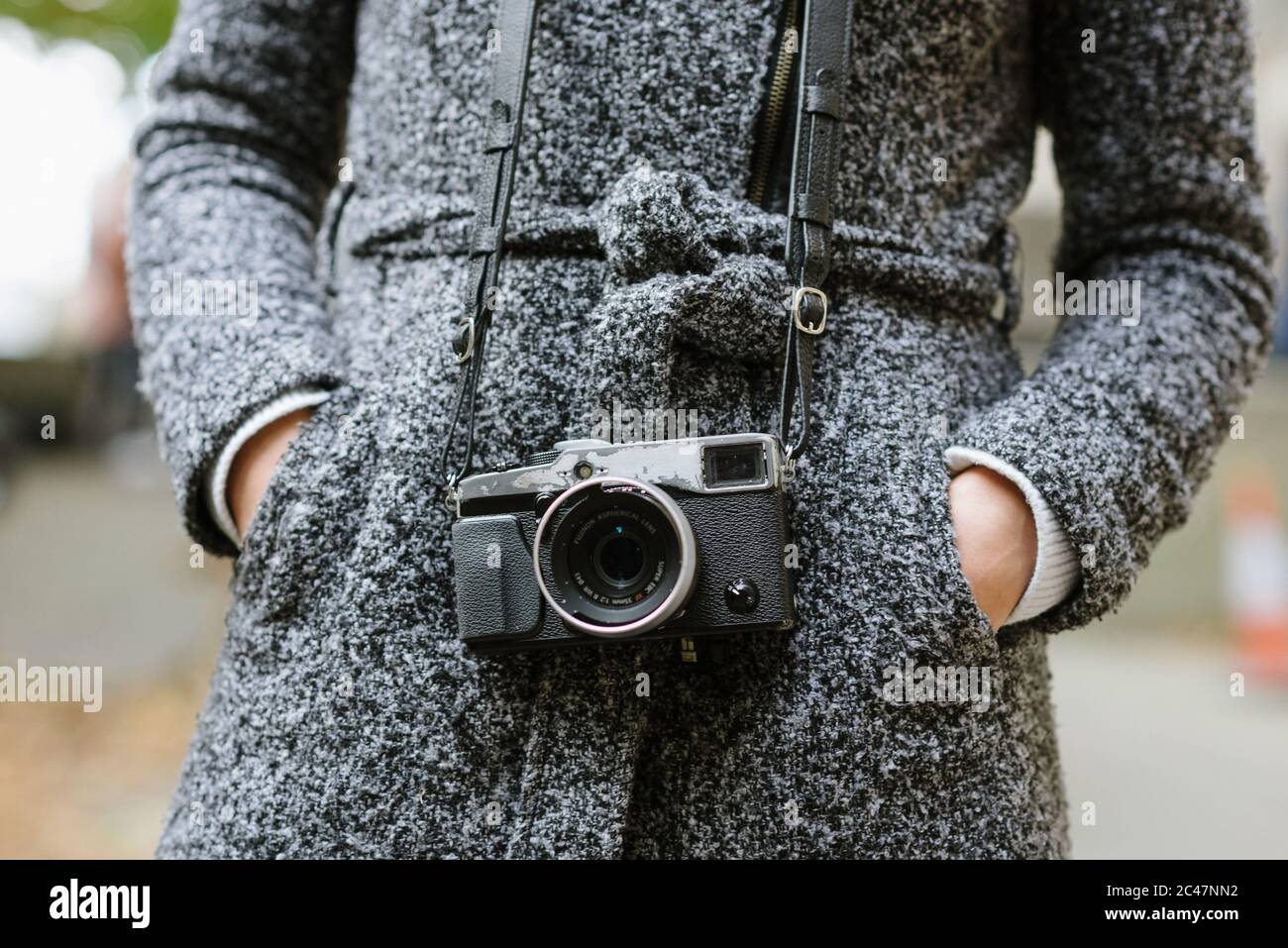 Colpo di una donna in piedi con le mani in lei tasche con un cappotto grigio e una fotocamera vintage Foto Stock