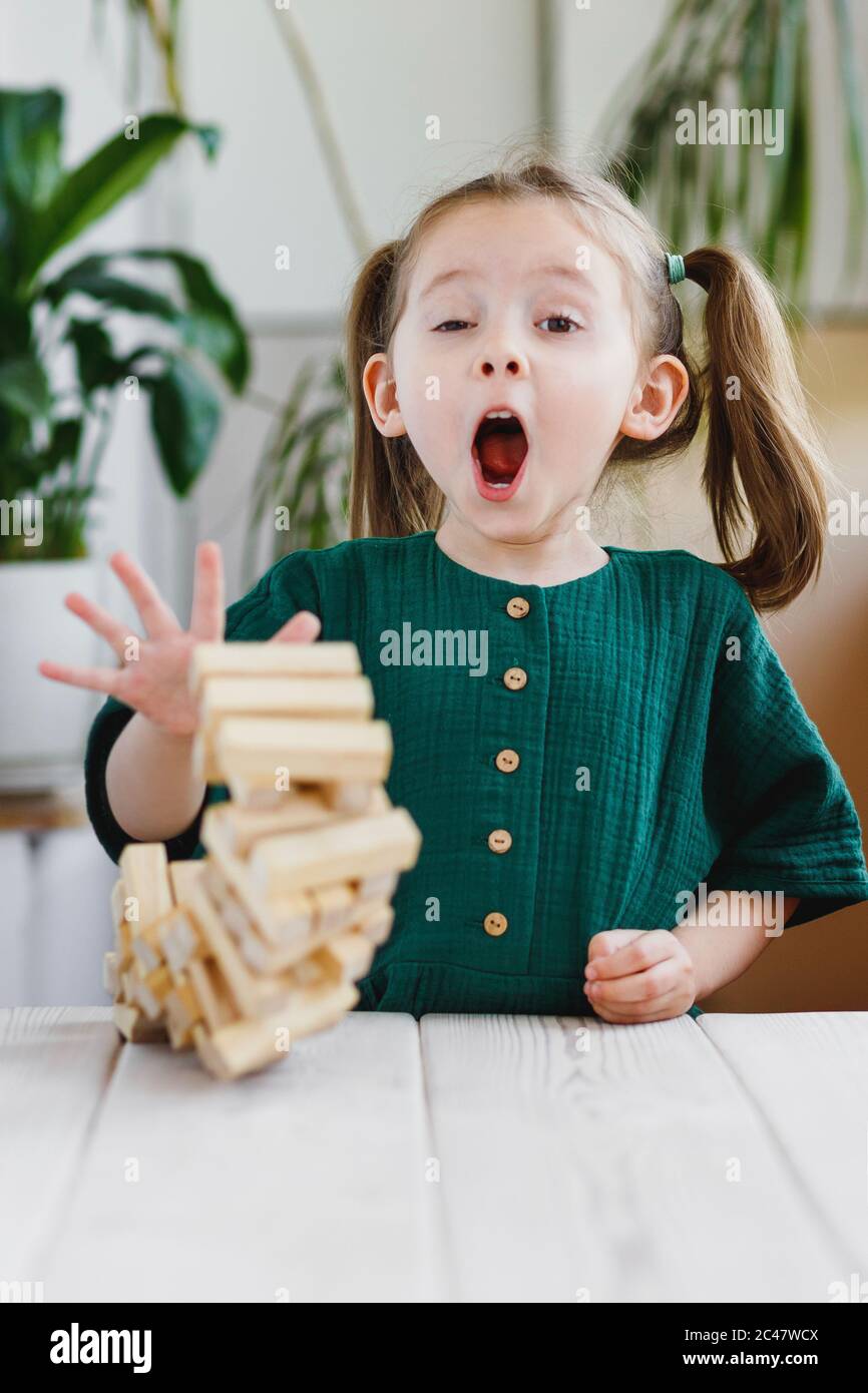 Prescolare età ragazza reazione espressiva su inaspettata caduta di blocco torre di legno Foto Stock