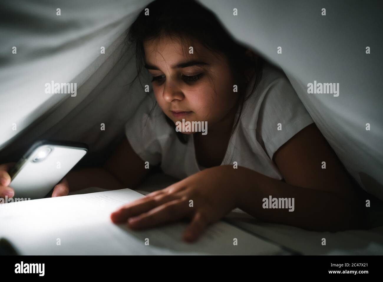 Bella ragazza caucasica che legge sotto i fogli bianchi con la torcia del  telefono cellulare in modo da lei può vedere Foto stock - Alamy