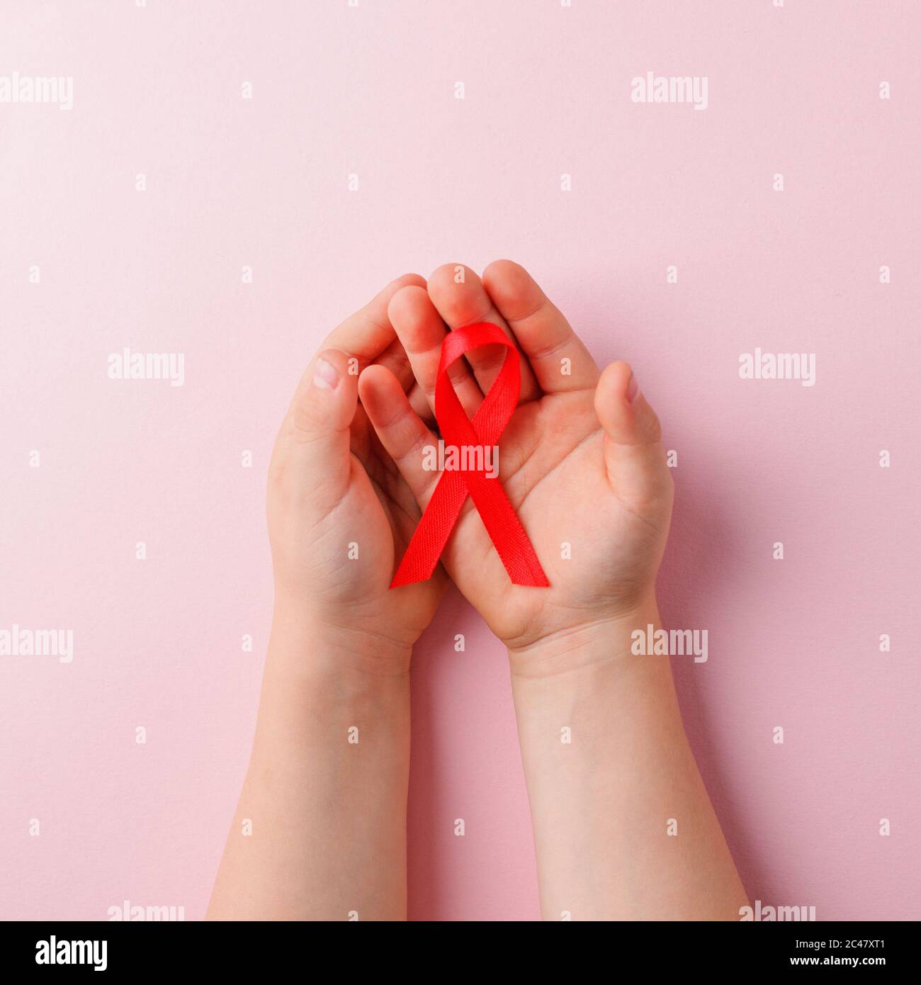 Concetto di salute e medicina - mani dei bambini che tengono rosso nastro di consapevolezza dell'AIDS su rosa, banner per il mese nazionale dei donatori di sangue nel mese di gennaio, World AIDS d Foto Stock