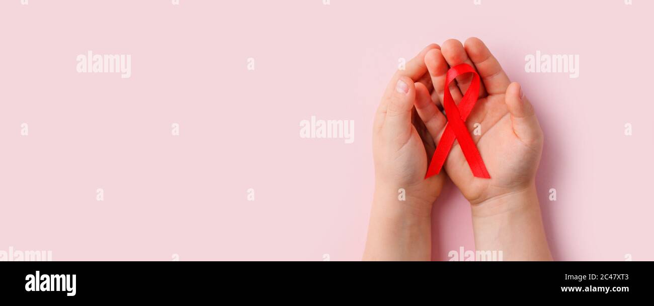Concetto di salute e medicina - mani dei bambini che tengono rosso nastro di consapevolezza dell'AIDS su rosa, banner per il mese nazionale dei donatori di sangue nel mese di gennaio, World AIDS d Foto Stock