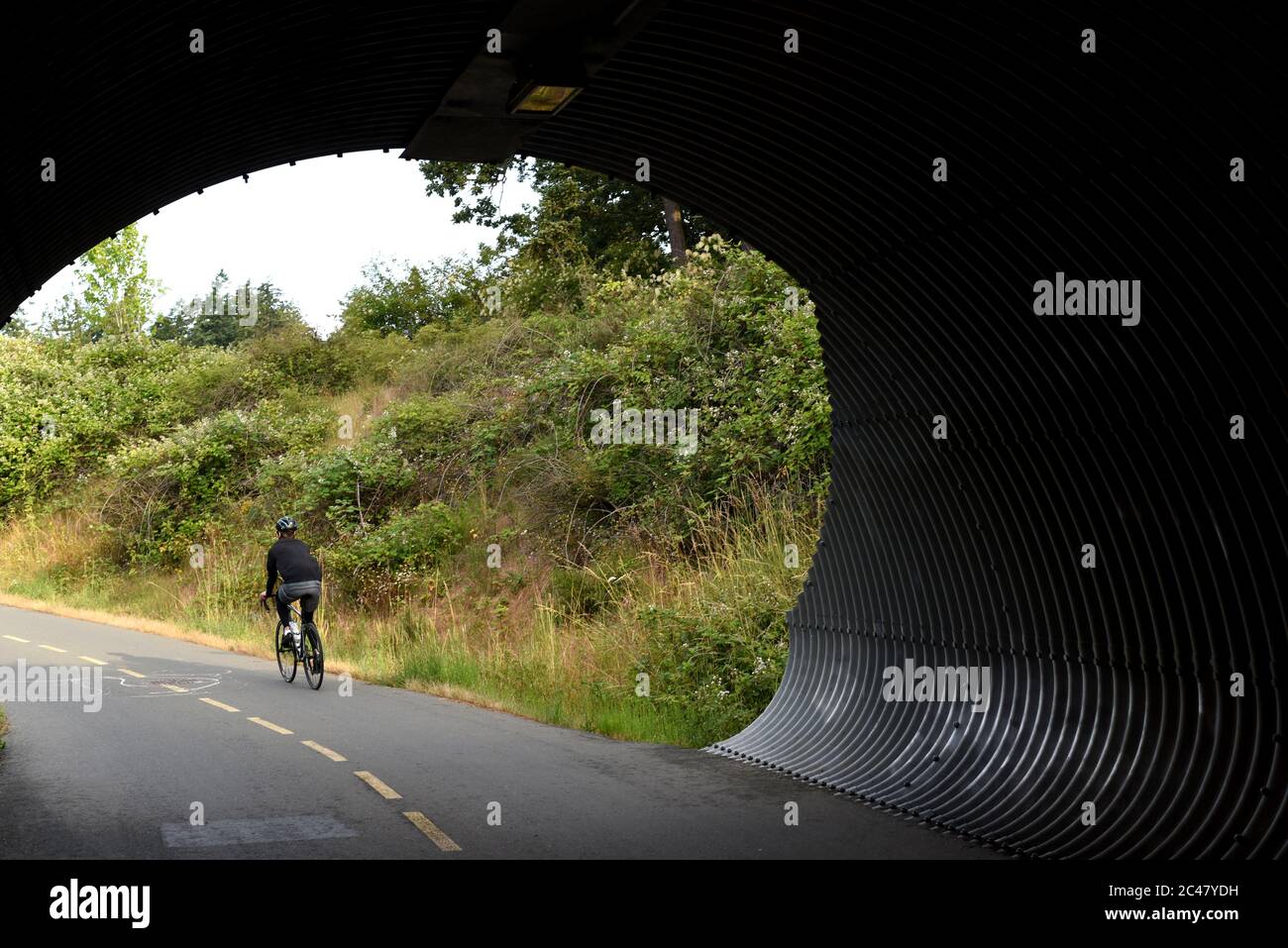 Una bicicletta ciclista da un tunnel sul Galloping Goose Trail nella grande città Victoria di View Royal. Il vecchio sentiero ferroviario è utilizzato da pedoni Foto Stock