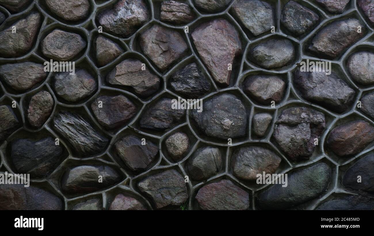 Parete colorata in pietra e cemento. Mosaico di rocce usate come tessere. Recinzione in pietra scura di colore chiaro. Struttura decorativa in materiale naturale Foto Stock