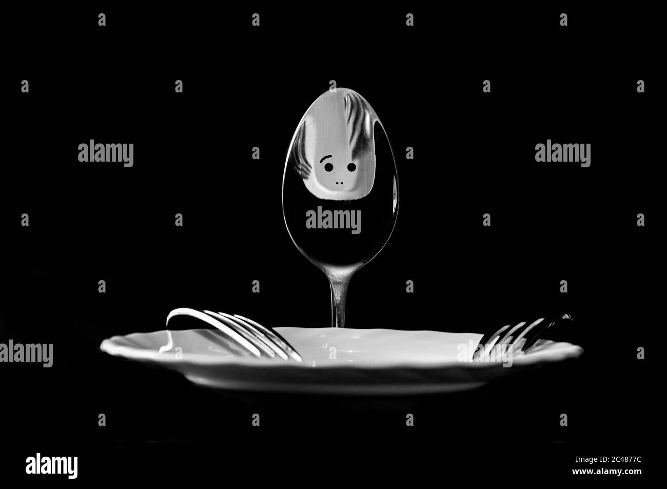 foto di un cucchiaio con occhi e bocca e forcelle con un piatto in forma di uomo su fondo nero Foto Stock