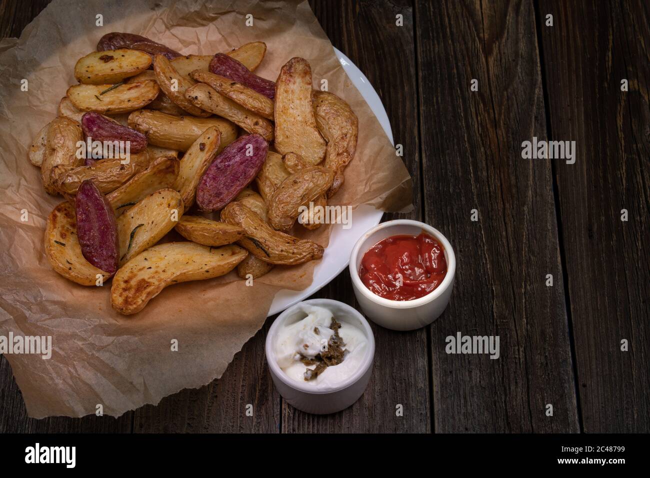 Fritti d'aria fritti di patate porpora e giallo zeppe servite con crema e ketchup su tavolo di legno, spazio copia Foto Stock