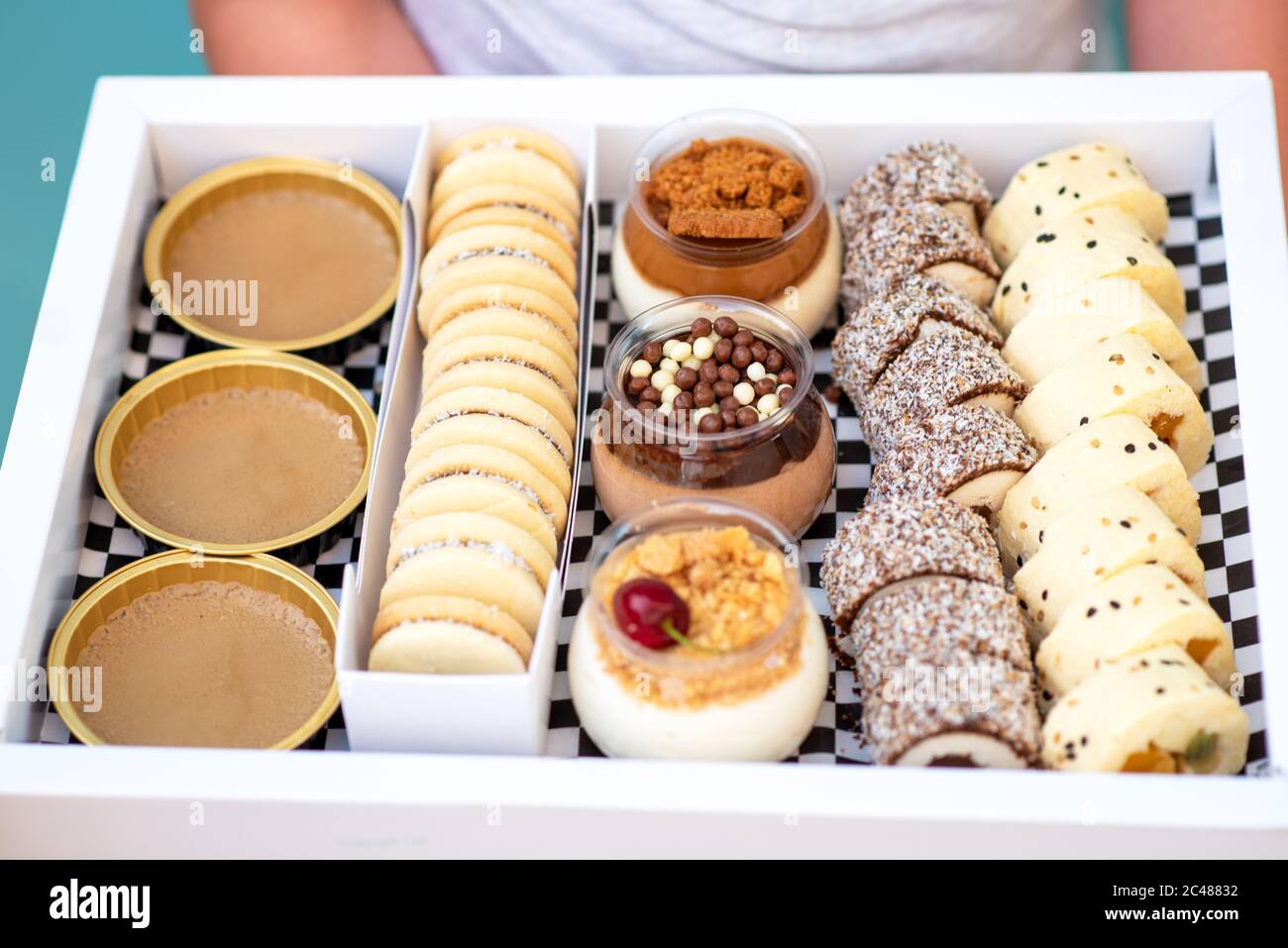 Deliziosa mousse al cioccolato e alla vaniglia decorata con crema dolce, biscotti e caramelle in un vaso di vetro. Sushi di frutta fresca, alfajores, macaroon e creme brulee in scatola bianca. Happy hour, consegna a domicilio. Foto Stock