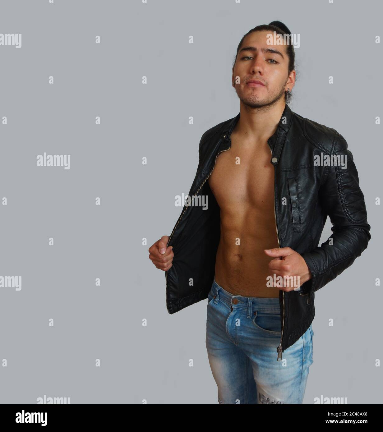 Giovane ispanico con i capelli raccolti fiocco in giacca nera di pelle senza camicia, con le mani che allungano la giacca, guardando verso la macchina fotografica Foto Stock